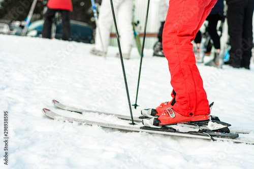 Sport set of skis, boots and sticks in red on woman's leg close up.