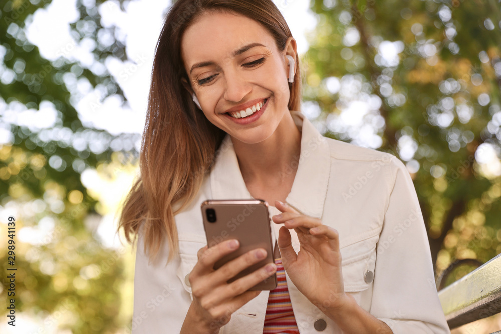 Young woman with wireless headphones and mobile device listening to music in park Young woman with wireless headphones and mobile device listening to music in park