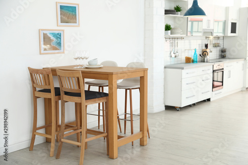 Stylish kitchen interior with dining table and bar stools near white wall