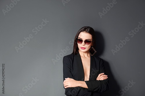 Beautiful woman wearing jacket and sunglasses on black background, space for text