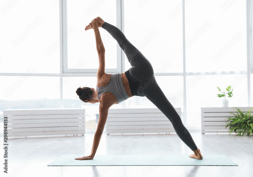 Young woman practicing extended side plank asana in yoga studio, back view. Utthita Vasisthasana pose