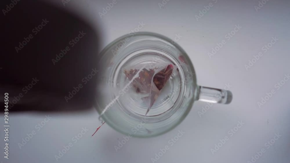 man brews delicious red raspberry tea bag in glass mug pouring hot water from kettle close upper view slow motion