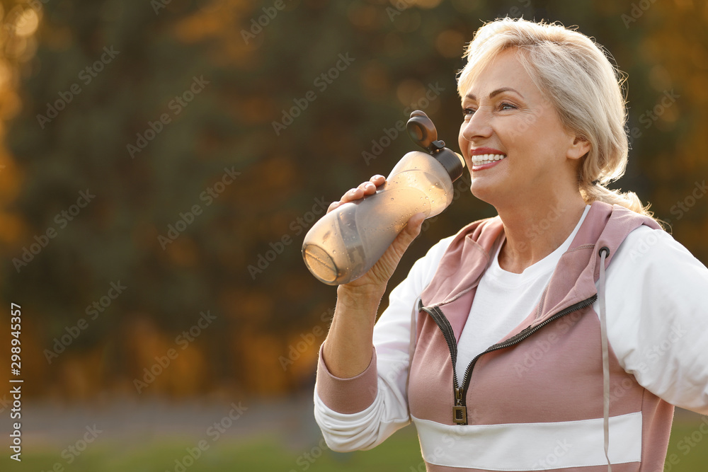 Sporty mature woman with bottle of water outdoors - obrazy, fototapety, plakaty 