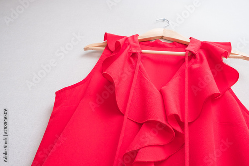 red women's blouse on wooden hanger against gray wall