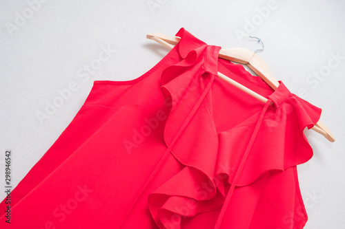 red women's blouse on wooden hanger against gray wall