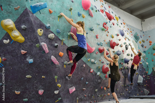 Group of three young sportswomen in activewear exercising on climbing wall