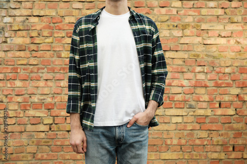 Men in white t-shirt and checkered shirt against brick wall, copy space