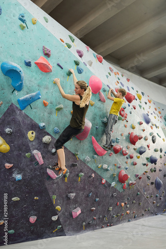 Active woman and her son in sportswear climbing wall with small artificial rocks