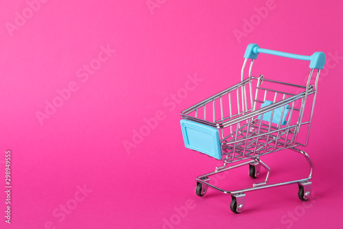 Small shopping cart on pink background, space for text