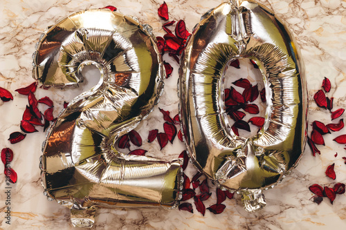 number 20 twenty in the form of silver balloons  on marble background decorated with dry petals. Happy anniversary card. Happy birthday balloon banner. Holiday decoration.