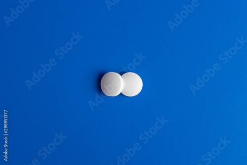 two white round pills on a blue background. Flatlay