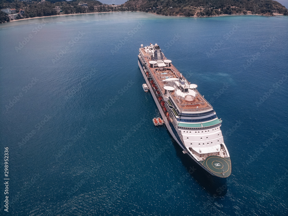 Aerial shot of the huge cruise liner, blue water and coastline on the background; luxury relaxation.