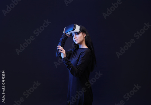 Woman in VR helmet scrolling invisible screen while interacting with virtual reality under neon light. Girl in glasses of virtual reality. Augmented reality, game concept. Dark background.