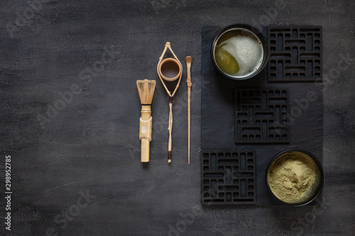 Matcha green tea ceremony kit - matcha powder, wooden spoon, strainer and whisk on a dark gray background