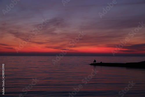 silhouette of a fisherman at sunset or sunrise. Bright colors of the sunset. Red sunset.