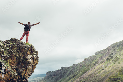 Male traveler stands on top of a mountain with open arms and enjoys the scenery