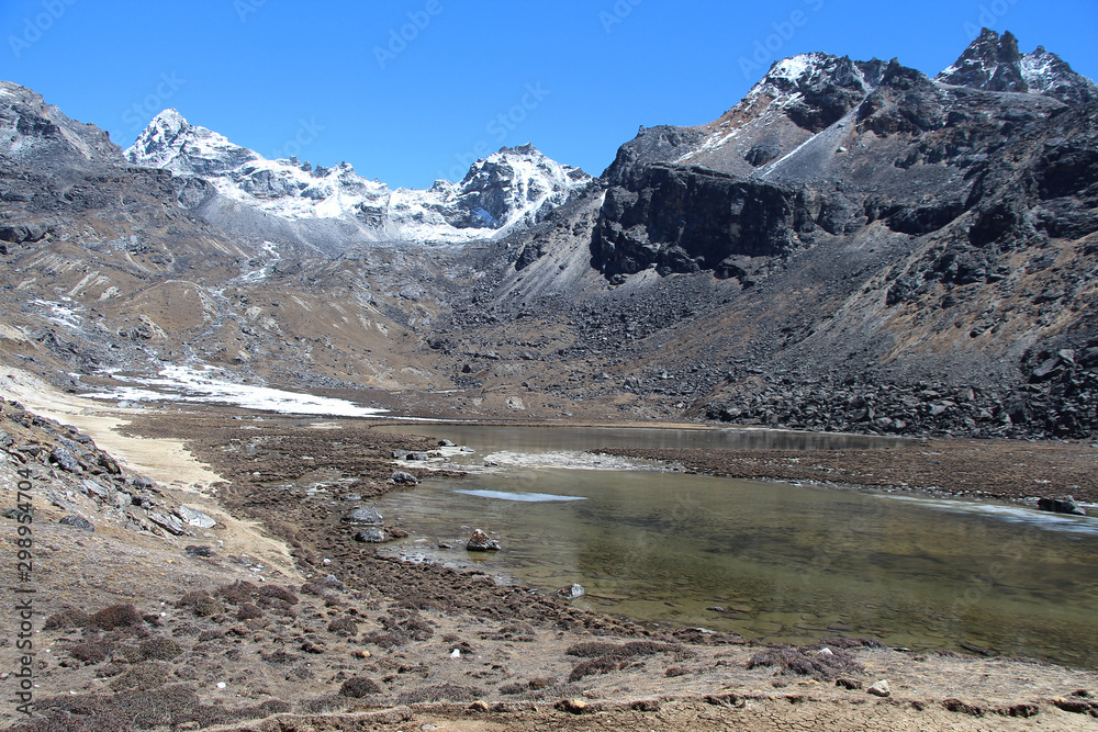 Lake Renjo at an altitude of about 4900 meters in the Himalayas near the Renjo Pass in Sagarmatha National Park in Nepal. Blue sky and white clouds over the mountain peaks and lake.