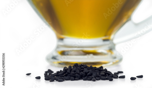 A handful of black cumin seeds on the background of a glass gravy boat with black seed oil. Selective focus. Isolated on white. photo