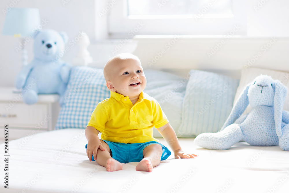 Baby boy playing on bed in sunny nursery Baby boy playing on bed in sunny nursery