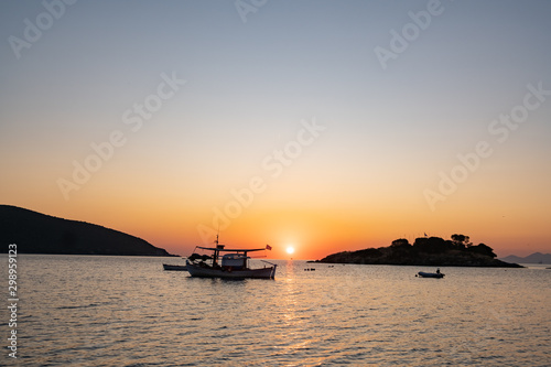 fishing boat with greece flag, beautiful sunrise on background © serejkakovalev