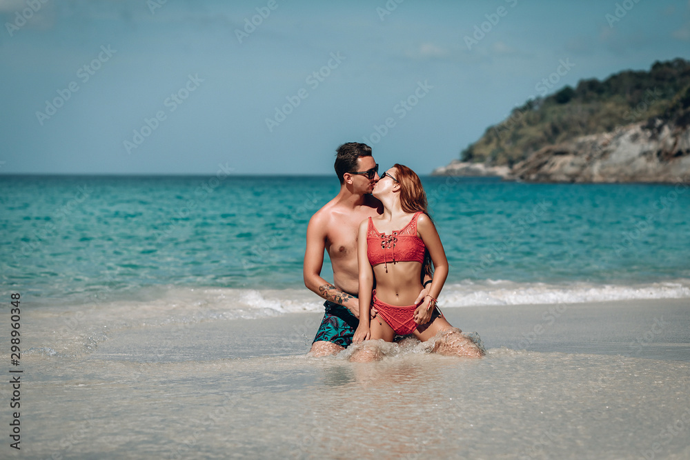 Loving couple sitting on the wet sand near the ocean kissing and hugging; honeymoon concept.