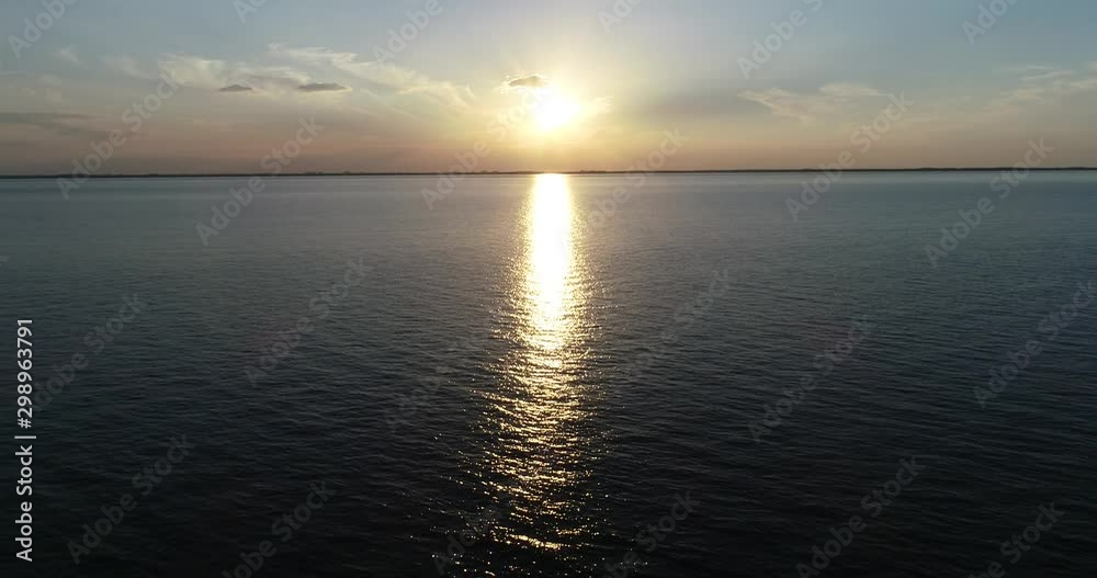 Aerial drone scene flying over water towards sun at sunset, golden hour. Reflection, coloured clouds. Las Cañas, Rio Negro, Uruguay Aerial drone scene flying over water towards sun at sunset, golden hour. Reflection, coloured clouds. Las Cañas, Rio Negro, Uruguay