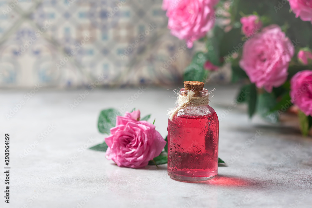 Natural pure rose oil or scented water in bottles for spa, skin care or aromatherapy. Glass bottle on a wooden table, small pink roses with leaves. Organic cosmetics concept. Natural pure rose oil or scented water in bottles for spa, skin care or aromatherapy. Glass bottle on a wooden table, small pink roses with leaves. Organic cosmetics concept.