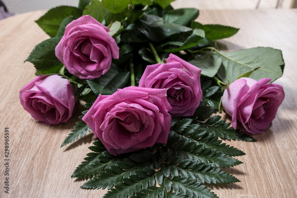 Five pink roses lie on a light oak table
