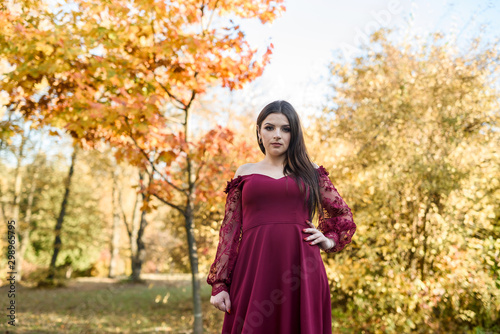 Young princess  in a beautiful red dress in park. The background is bright, golden autumn nature.