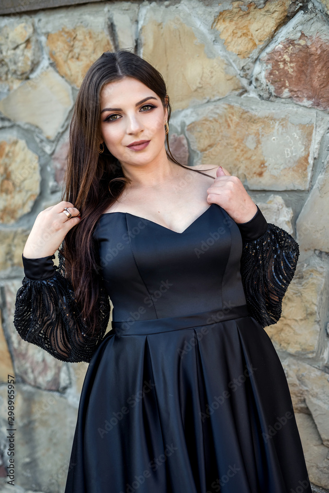 Fashion smiling woman in black dress on a brick background. Fashion