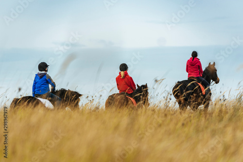 Quadro em tela Family Horseback riding during autumn day with tall grass foreground
