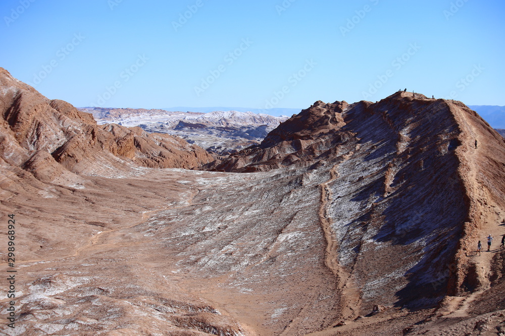 Atacama desert, Chile, with colored mountains in the foreground. Mountains and blue sky in the background.
