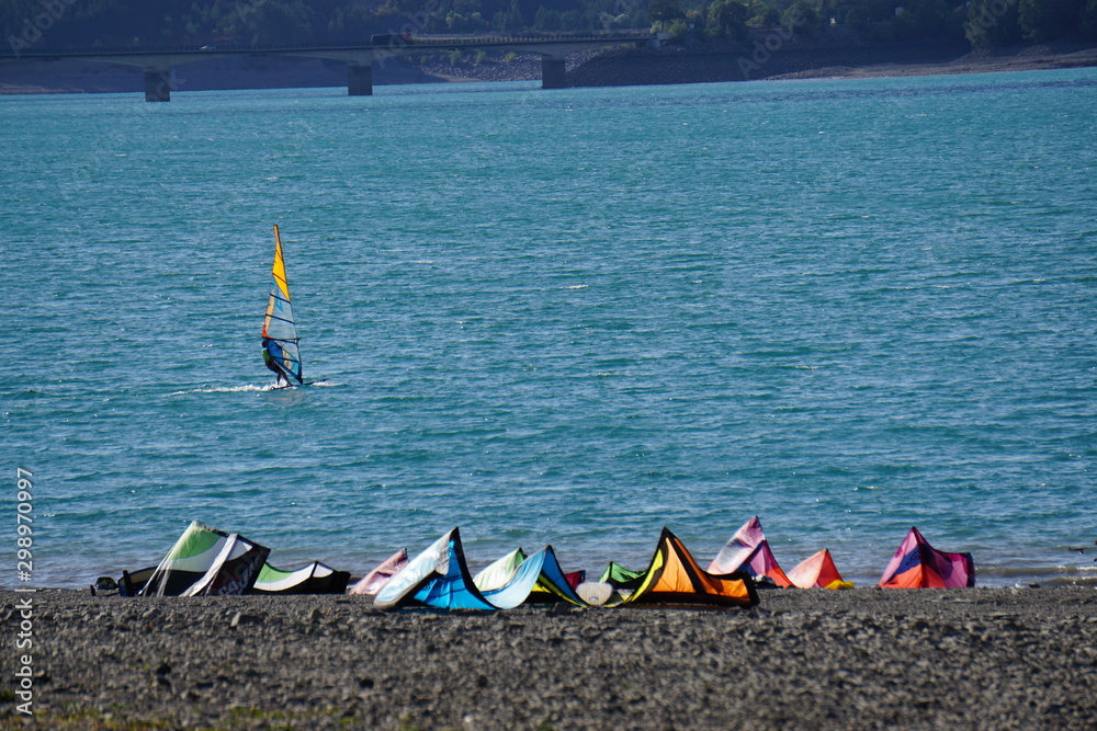 colorful sails on the beach with windsurfer on lake Serre Ponçcon, France