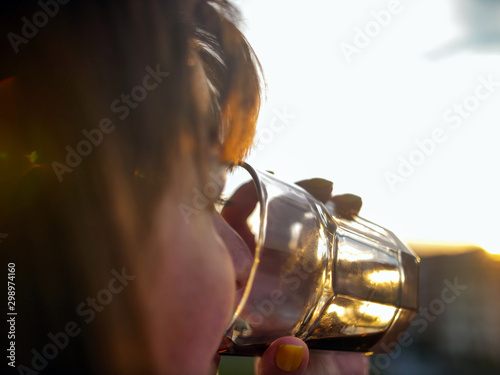 Woman drinks from a glass a drink at sunset background, close-up, sun glare