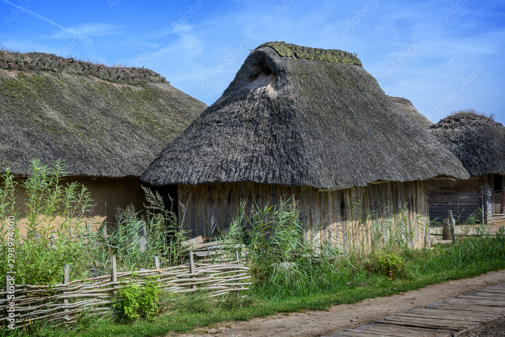 Historical wooden house with thatched roof in the reconstructed Viking village Haithabu on the banks of the inlet Schlei of the Baltic Sea in Northern Germany, blue sky, copy space