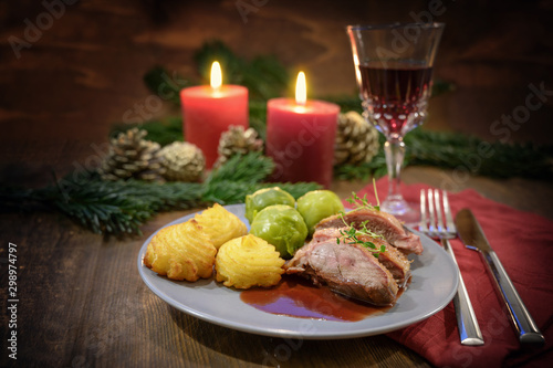 duck breast with duchess potatoes, brussels sprout and sauce, served as a festive christmas dinner with red wine, napkin and burning candles on a dark wooden table, copy space