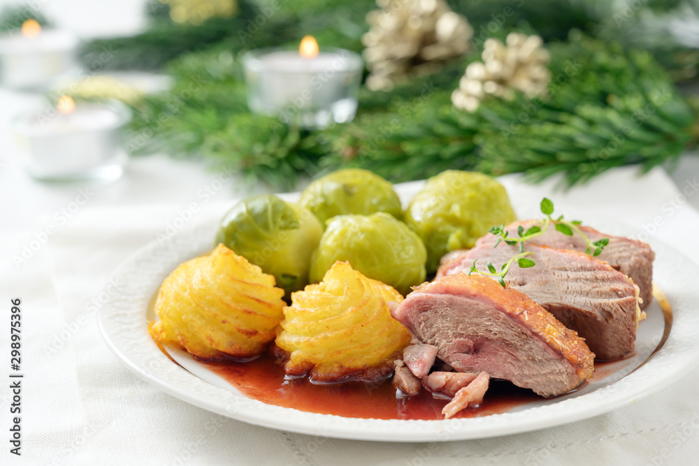 Christmas dinner, seared duck breast fillet with duchess potatoes and brussels sprout on a white table with candles, fir branches and decoration