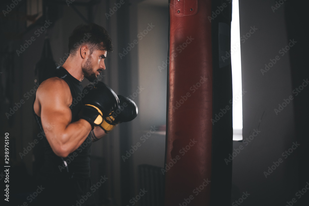 In a large cross fitness class young strong man with a perfect muscle boxing hard and concentrated wearing boxing gloves
