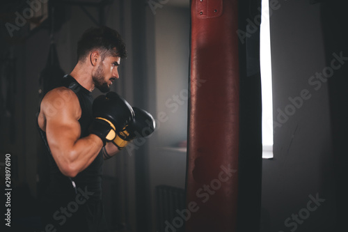 In a large cross fitness class young strong man with a perfect muscle boxing hard and concentrated wearing boxing gloves