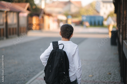 Back view of boy in white shirt with black backpack go home after the lesson