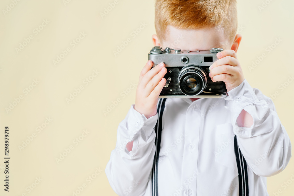 little red-haired boy with a retro camera in hands on an isolated light background little red-haired boy with a retro camera in hands on an isolated light background