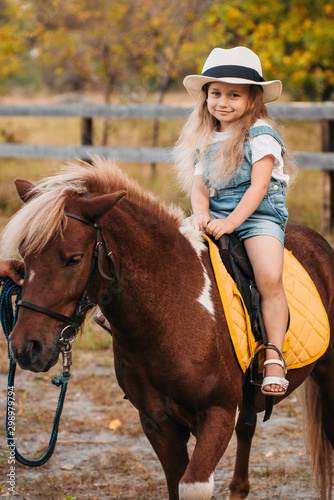 Adorable little girl riding a pony at summer