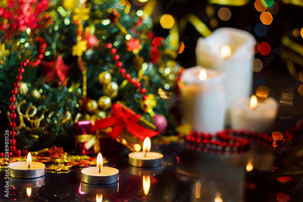 Candles are burning, decorated wreath, decor for christmas tree, presents, balls are on table. Festive decorative garland with multicolored light bulbs are shining on background. New year mood.