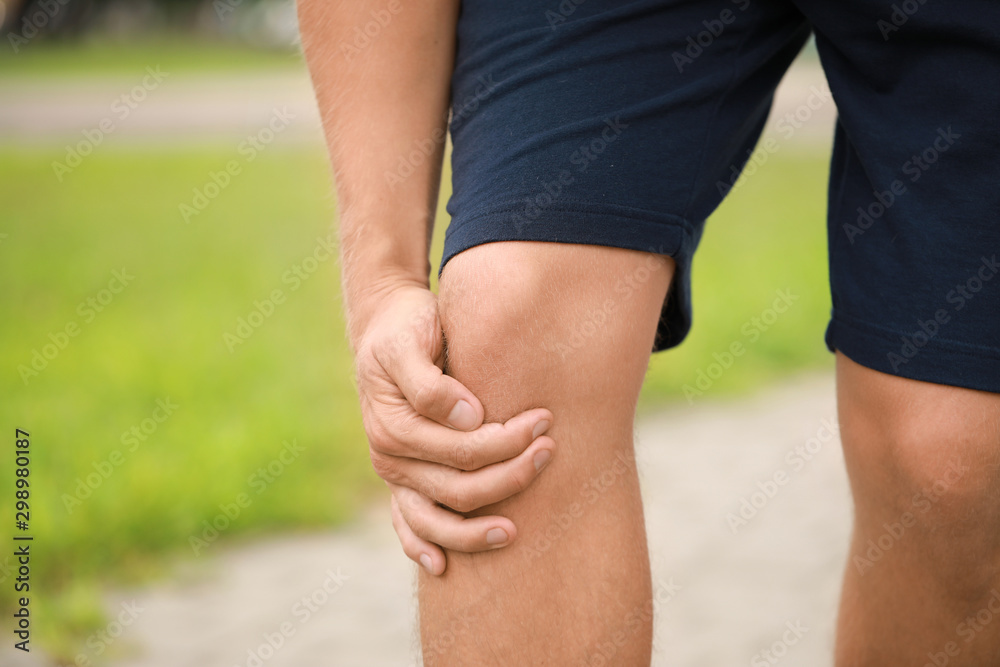 Young sporty man suffering from pain in knee outdoors, closeup Young sporty man suffering from pain in knee outdoors, closeup
