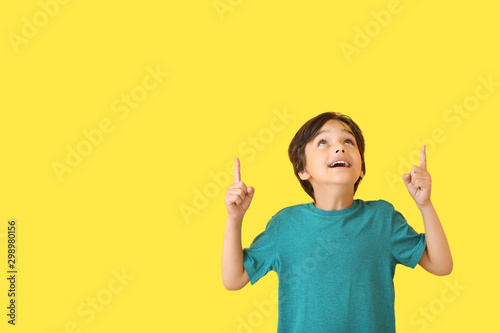 Happy little boy pointing at something on color background