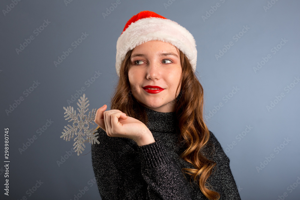 girl in santa hat portrait with big silver snowflake toy posing on gray color background, christmas holiday concept, happy and emotions on isolated gray background girl in santa hat portrait with big silver snowflake toy posing on gray color background, christmas holiday concept, happy and emotions on isolated gray background