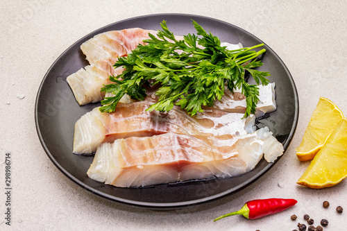 Raw pollock (Pollachius virens) pieces. Fresh fish for healthy food lifestyle. Lemon, parsley, sea salt, chili, black peppercorn photo