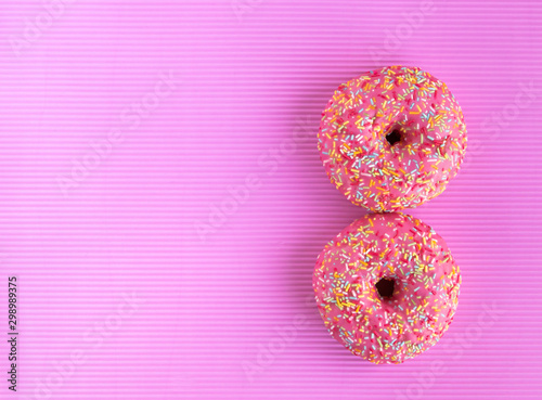 Donuts covered with pink icing and colored pastry topping on a pink background. Copy space.