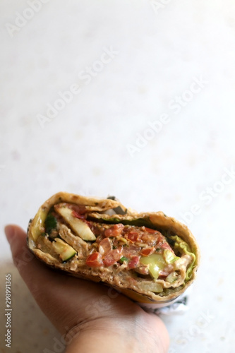 Holding a tortilla wrap with roasted vegetables, guacamole and sauce. Selective focus.