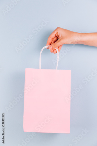 Female hand holding pink paper bag isolated on blue background